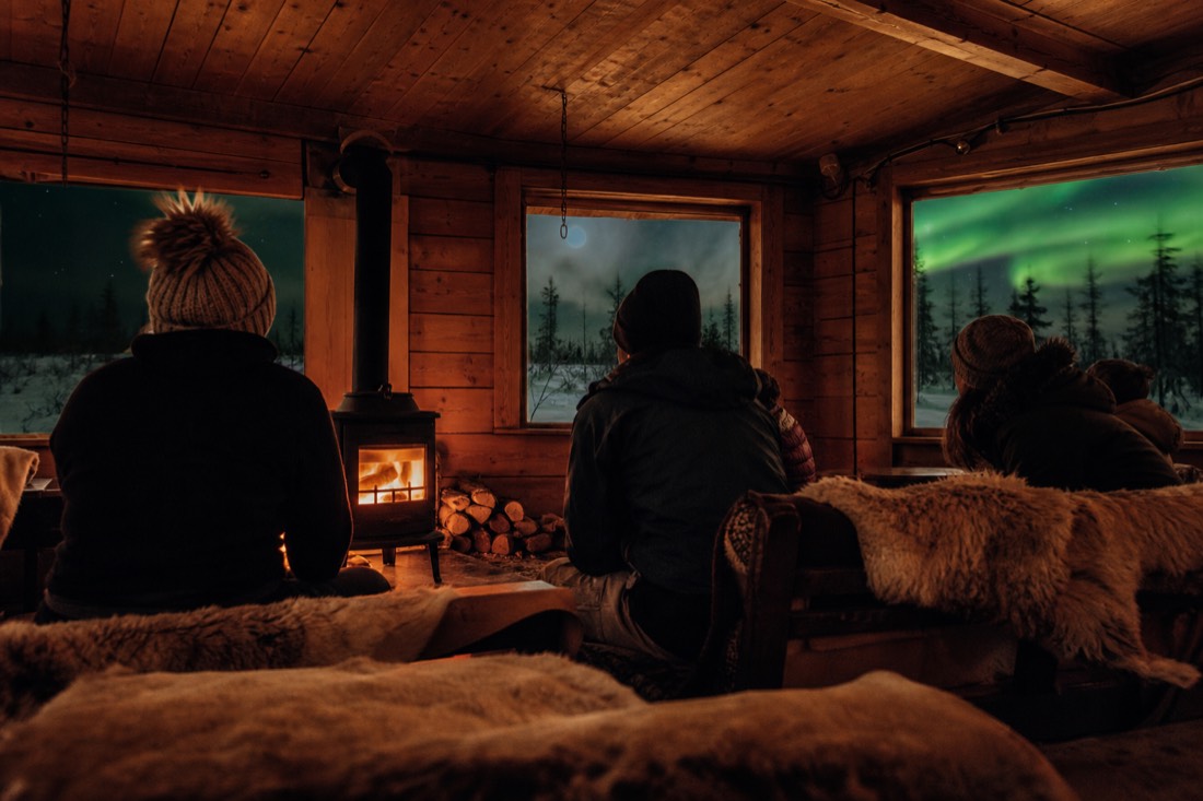 Guests listening to stories around a wood stove in a warm cabin after a dog sled ride