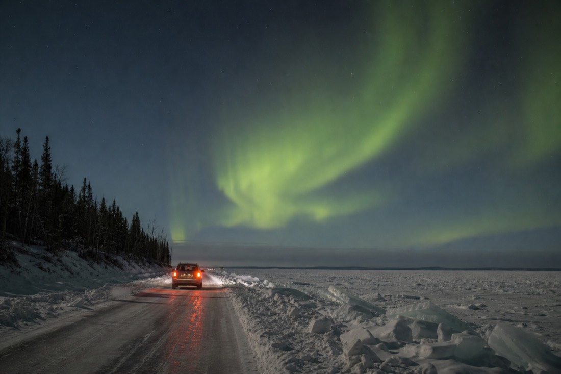 Regular passenger car driving the plowed Dettah ice road across the frozen bay with pressure ridges beside the lane