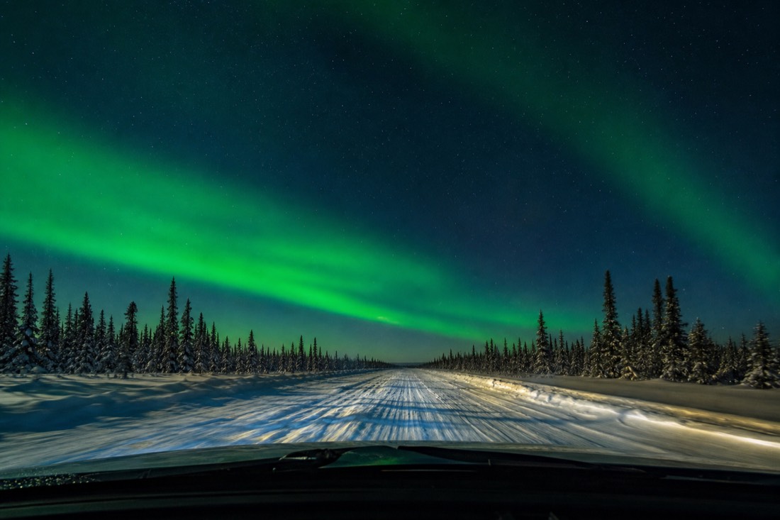 View through a windshield of the white ice road lane with wind-carved snow and blue shadows stretching ahead