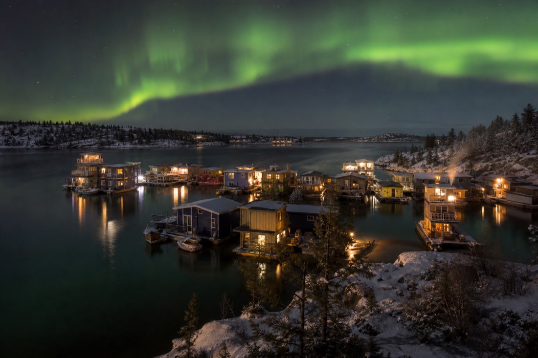 Cluster of colourful houseboats at anchor in Yellowknife Bay with woodsmoke rising on a still morning