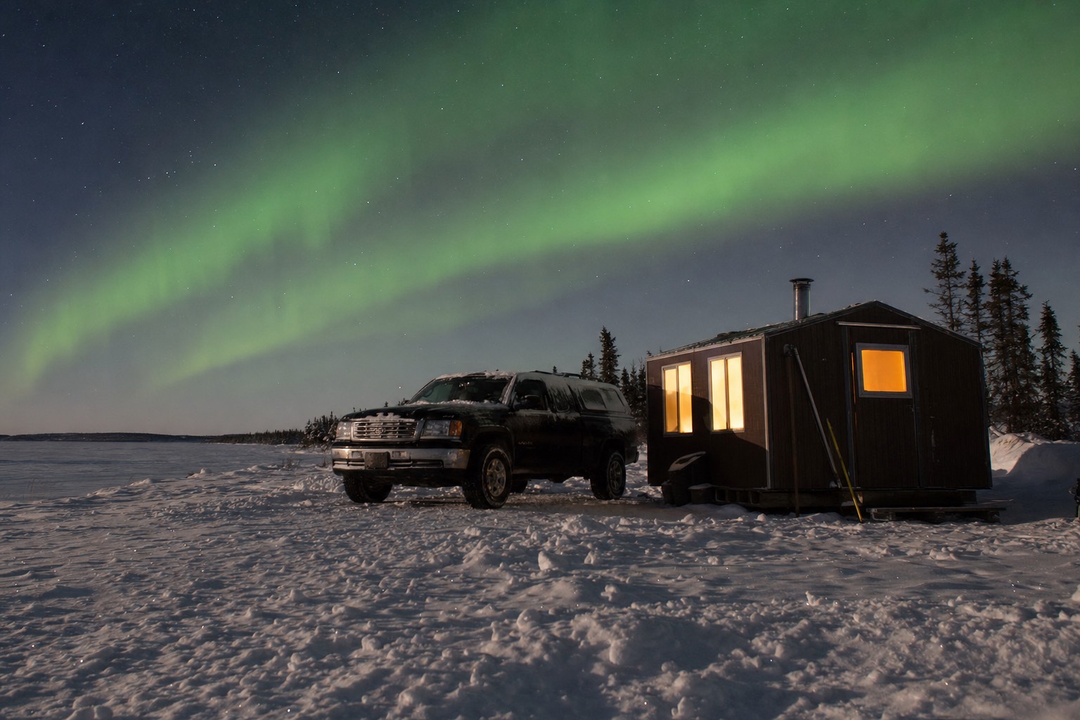 Heated ice fishing hut on frozen Great Slave Lake with a truck parked beside it under a pale winter sun