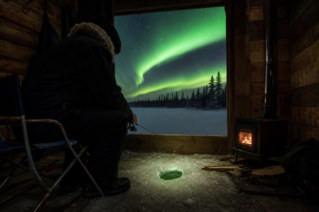 Visitor jigging a fishing rod over a drilled hole inside a warm ice fishing hut