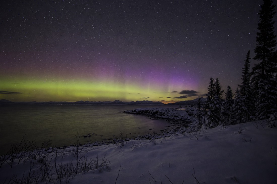 Faint pale aurora glow low on the horizon above coastal water during a strong geomagnetic storm