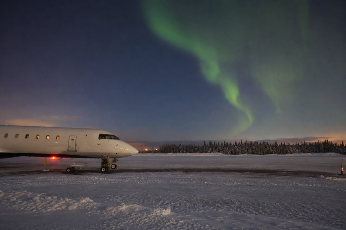 Small airliner on the snowy apron at Yellowknife airport at dusk with aurora beginning overhead
