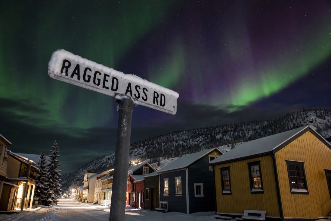 Snow-dusted street sign for Ragged Ass Road beside small colourful gold-rush era houses in Old Town