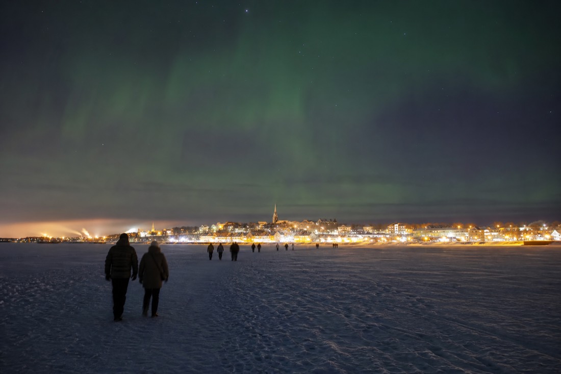 Visitors crossing the snow-covered bay ice toward Old Town at dusk with warm lights on the shoreline