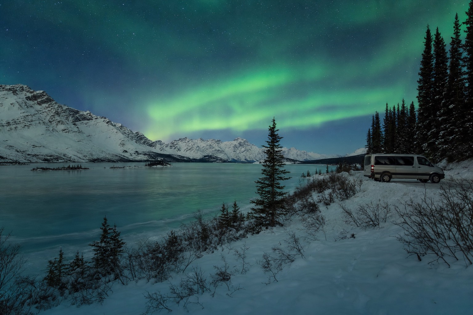 Green aurora arc over a frozen lake beside the Ingraham Trail with a tour van parked at the shoreline