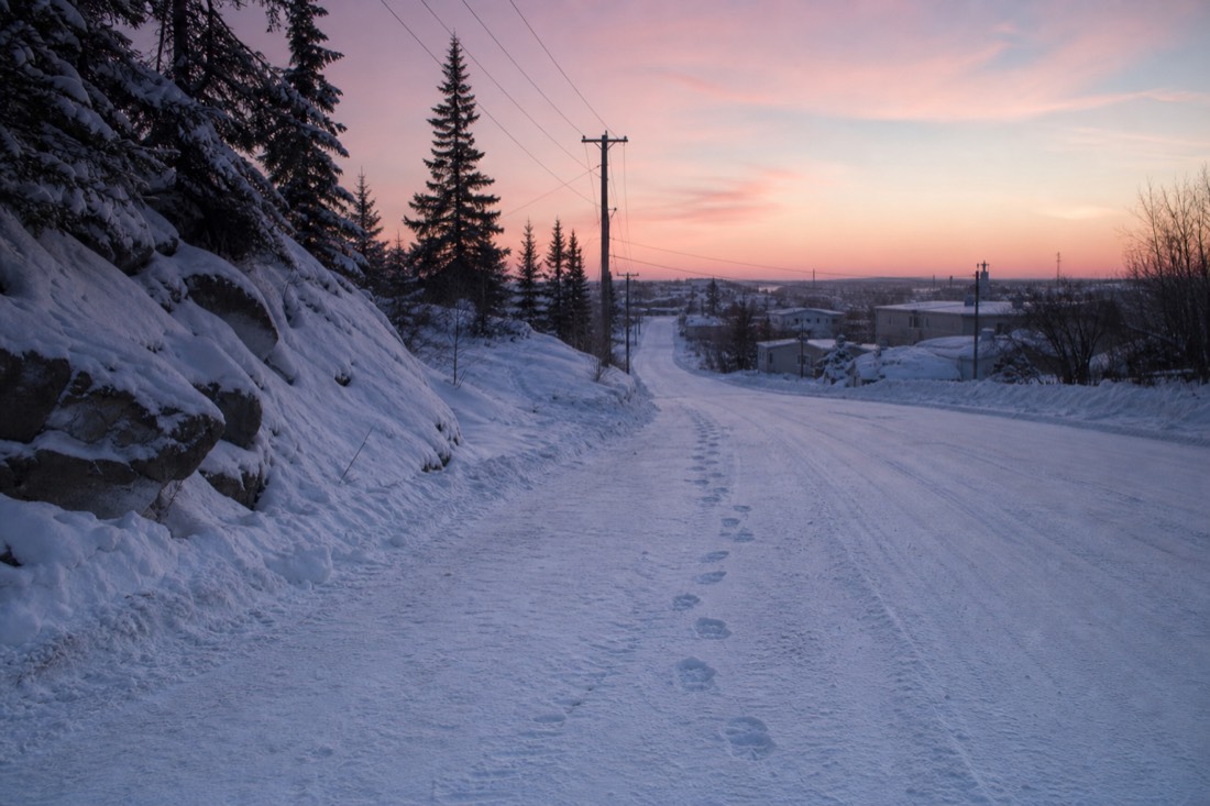 Boot prints in dry squeaky snow on a quiet Yellowknife road under pink morning light