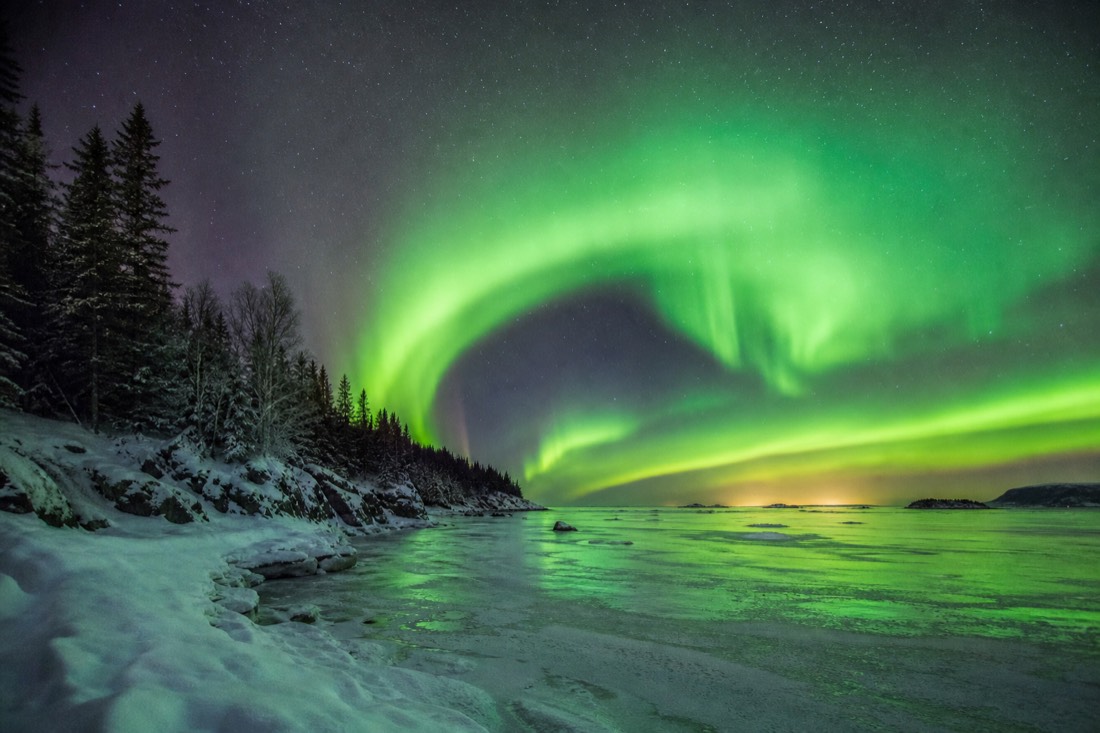 Bright green auroral arc filling the sky over a frozen bay on an otherwise quiet night