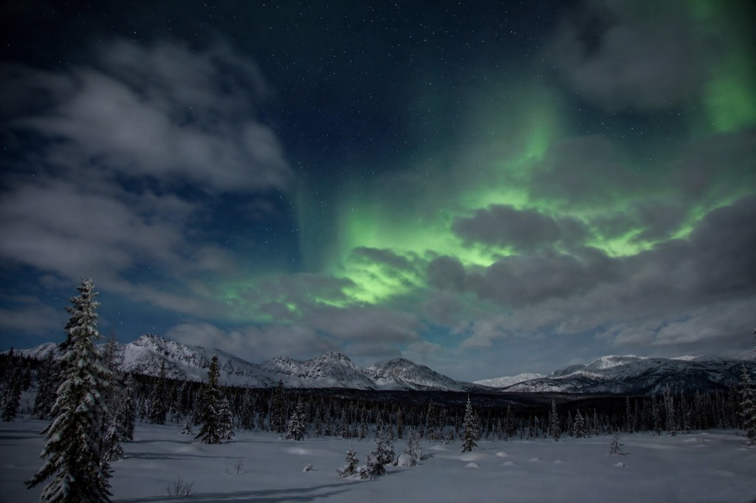 Broken cloud drifting across a starry sky with a pale green aurora glow visible through a clear gap