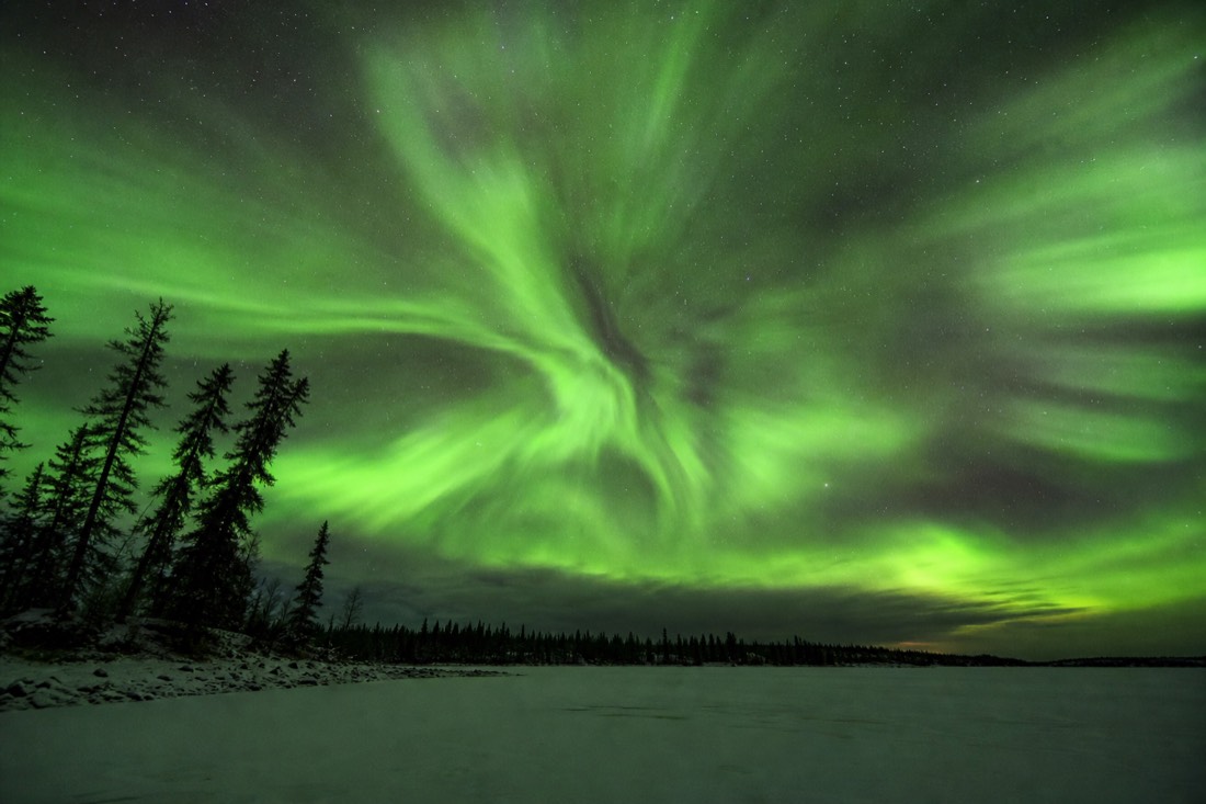 Bright green aurora corona directly overhead above a flat frozen lake outside Yellowknife