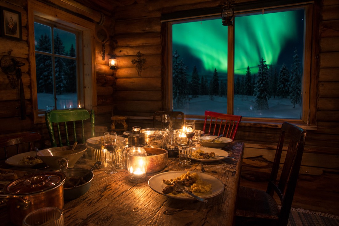 Cosy log-walled dining room with mismatched chairs and steam rising from plates on a winter evening