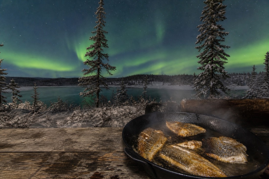 Pan-fried lake fish sizzling in a cast iron pan behind a well-worn wooden counter