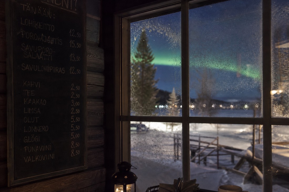 Handwritten menu board beside a frosted window in a northern cafe with snow falling outside