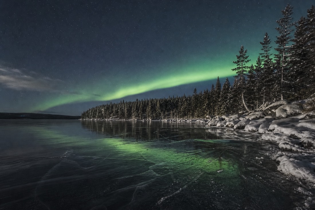 Soft but clearly visible aurora band on a calm low-activity night reflected on smooth lake ice