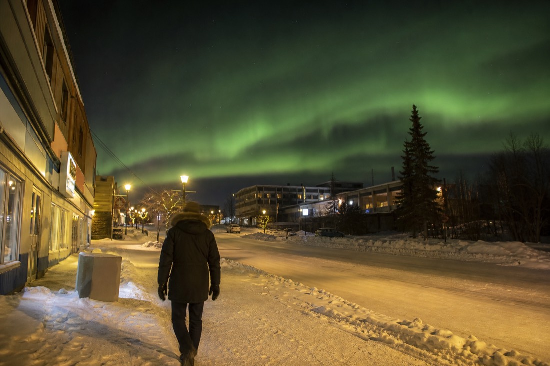 Visitor in a parka walking a snow-packed downtown Yellowknife street past low storefronts