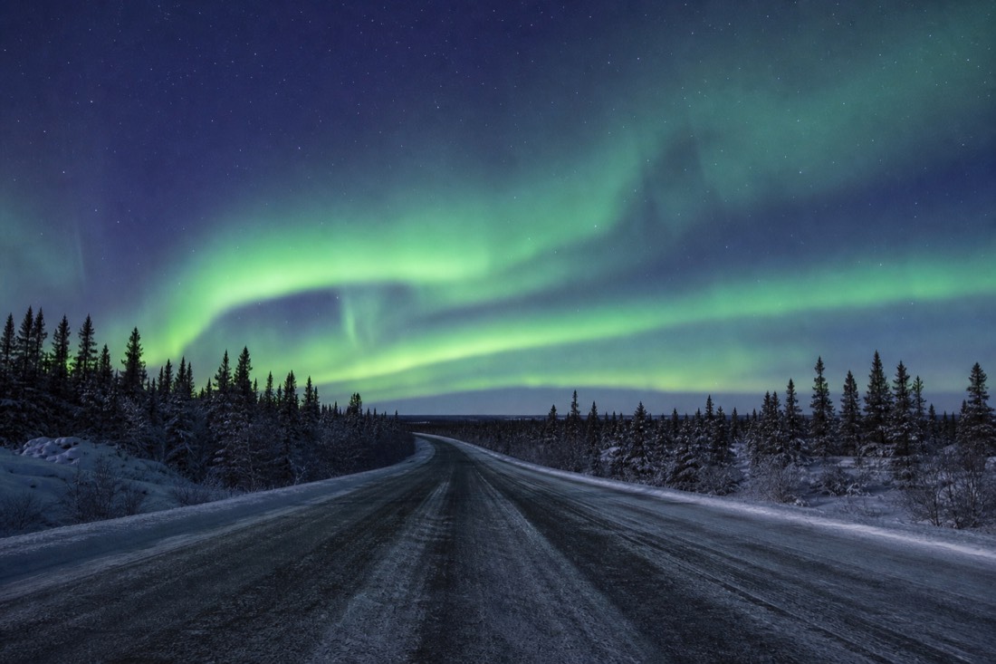 Empty two-lane Ingraham Trail highway cutting through snow-dusted spruce forest outside Yellowknife