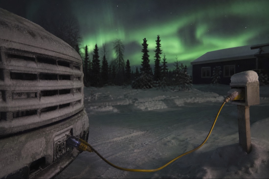Block heater cord running from a frost-covered car grille to an outdoor power outlet in Yellowknife
