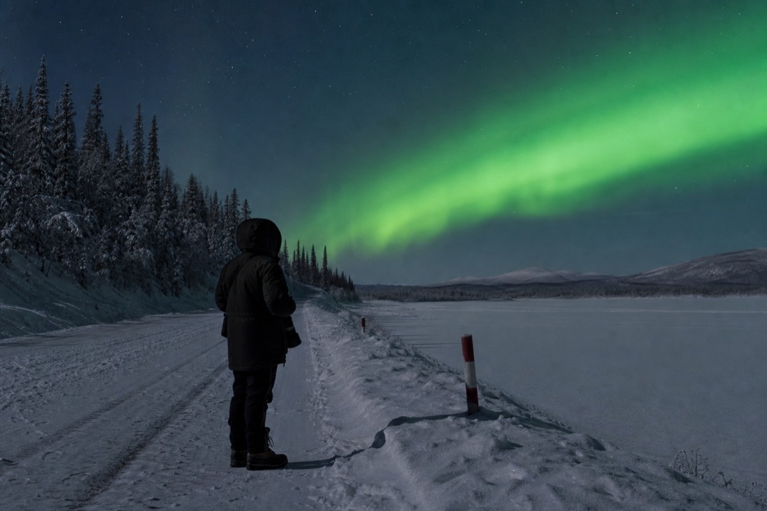 Lone photographer in full arctic clothing standing at the marked edge of an ice road at night