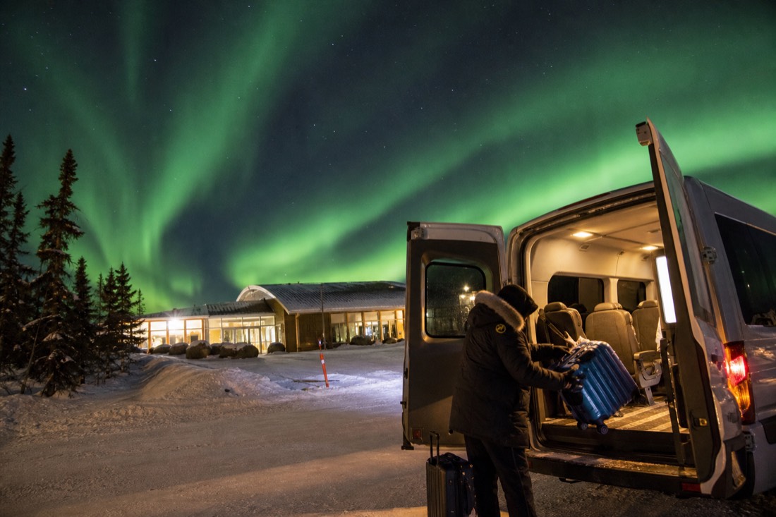 A traveler loading luggage into a warm shuttle van outside the small Yellowknife airport terminal in winter