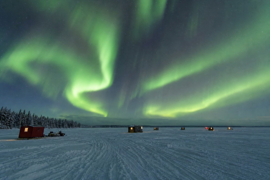Heated ice fishing huts scattered across frozen Great Slave Lake with snowmobile tracks between them
