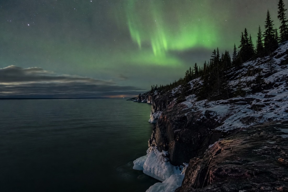 Dark deep water of Great Slave Lake meeting a steep rocky cliff shoreline under a wide northern sky