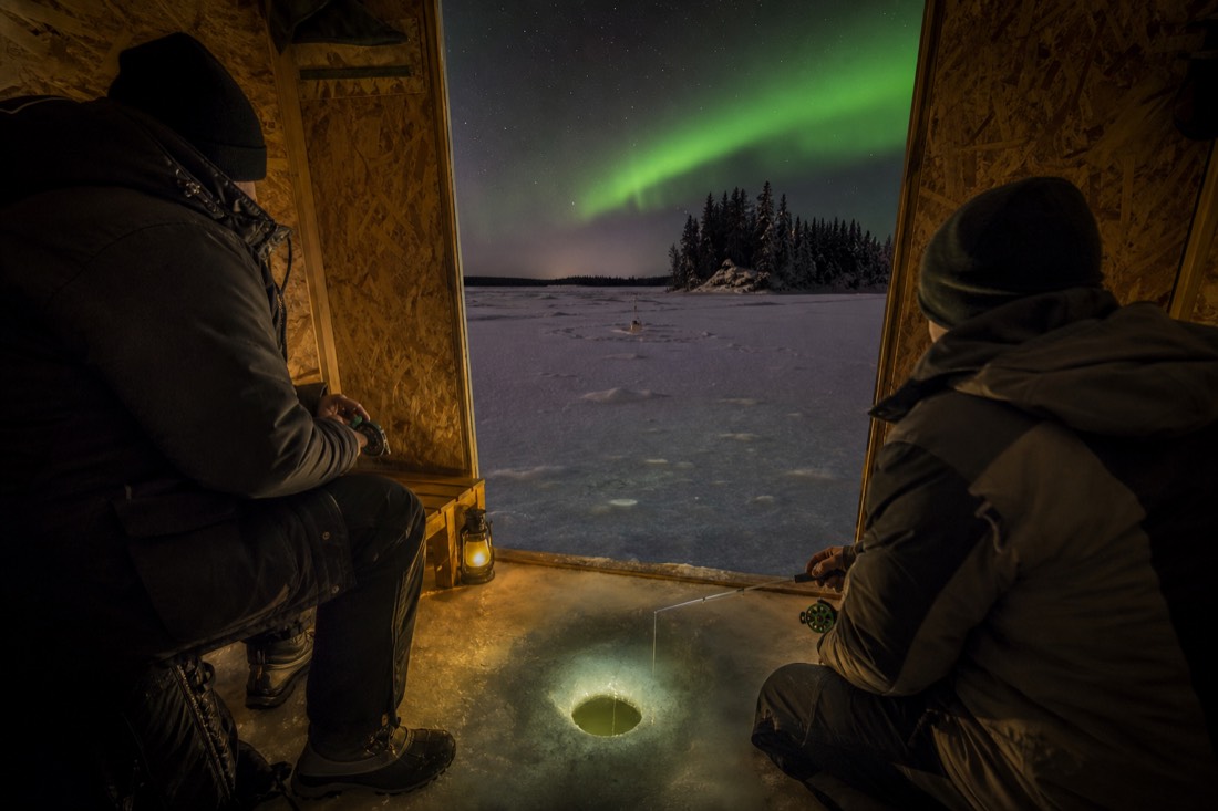 Group inside a warm ice fishing hut with a drilled hole in the floor and lines set on the frozen lake