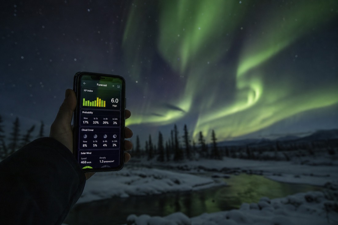Phone screen showing an aurora forecast app held up against a dark starry sky