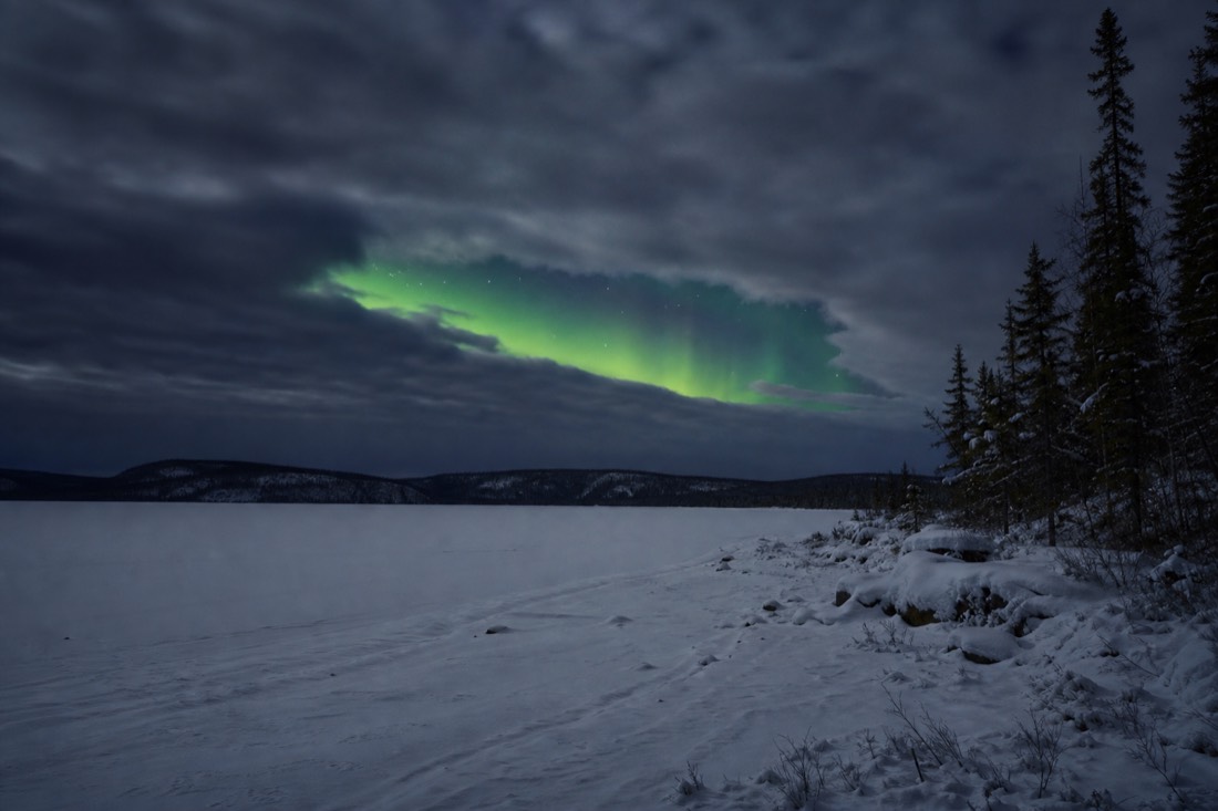 Break in heavy cloud over a frozen lake with a green aurora ribbon visible through the gap