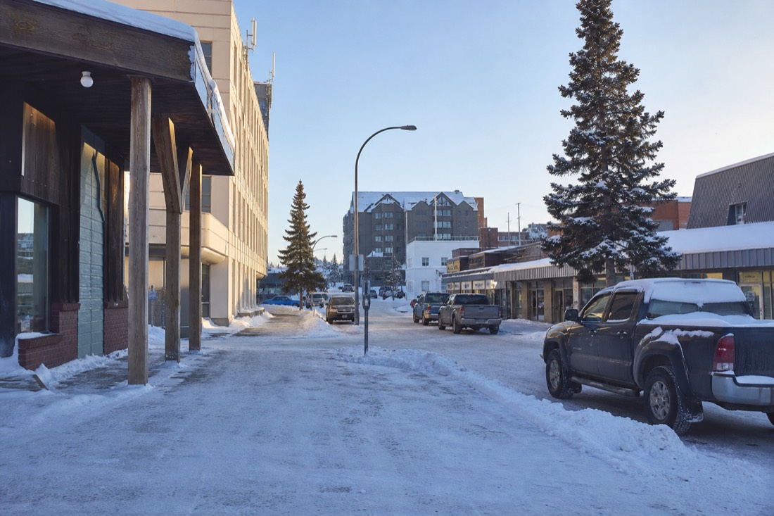 Downtown Yellowknife street corner in daytime winter light with parked trucks and low commercial buildings