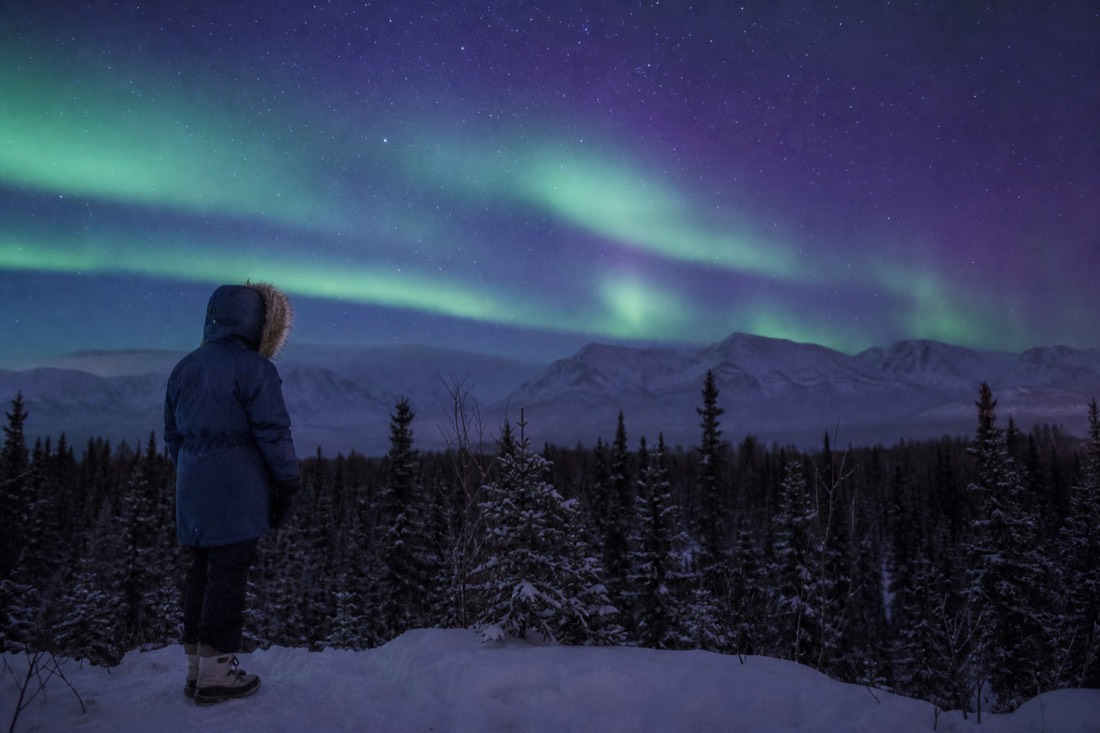 Traveler in a rented arctic parka and insulated boots smiling in deep cold with frost on their hood fur