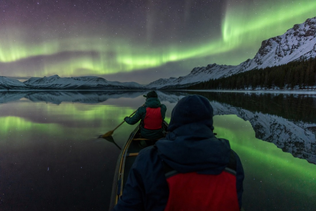Two people paddling a canoe on flat calm water under bright late evening light in midsummer