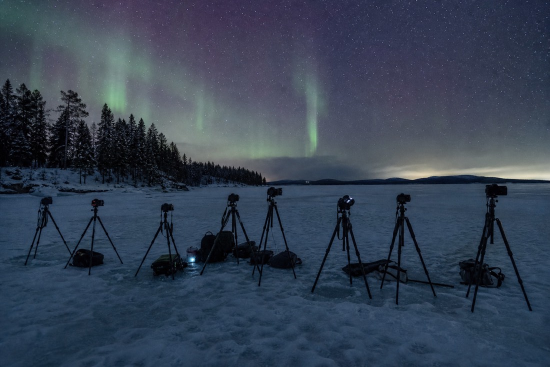 Row of tripods set up on a frozen lake near midnight with faint aurora beginning to brighten overhead