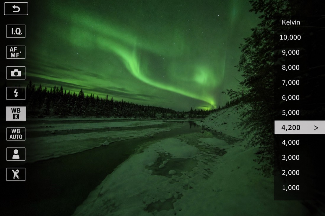 Camera menu screen showing a manual Kelvin white balance setting with green aurora light spilling across the frame