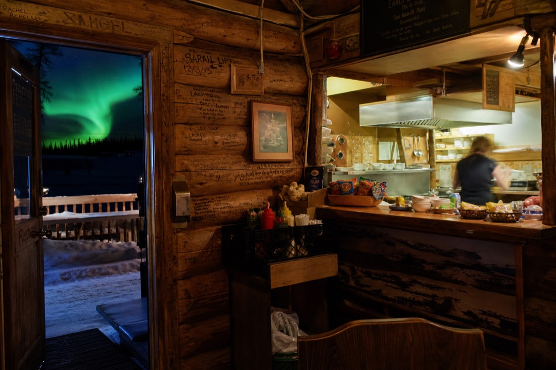 Interior of a cosy log cabin restaurant in Old Town Yellowknife with wooden walls covered in scrawled messages and a busy counter