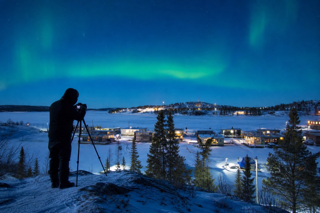 Photographer with a tripod on the rock above Old Town Yellowknife shooting the houseboats on the bay at blue hour