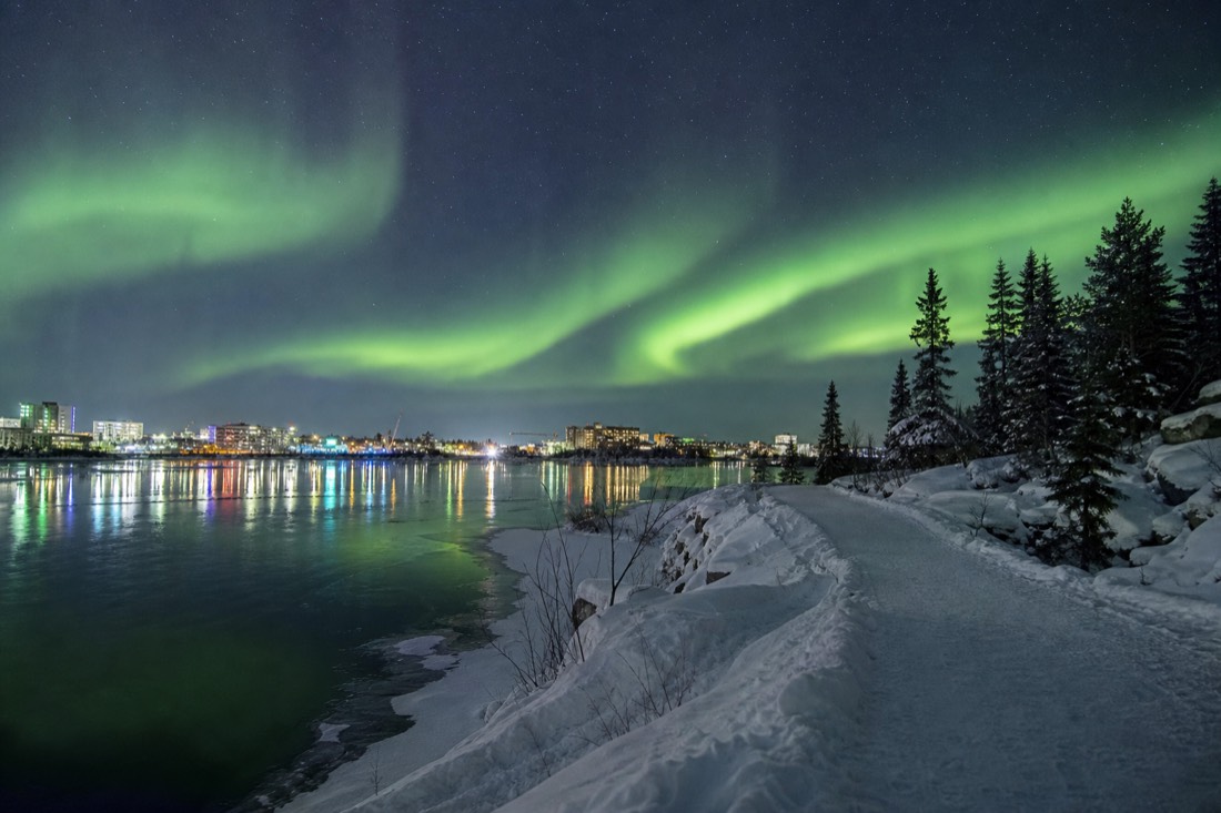 Lakeside walking trail curving along Frame Lake with downtown Yellowknife buildings across the water