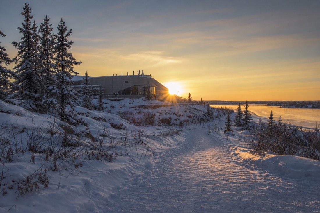 Snow-covered path leading to the lakeside museum in Yellowknife with low winter sun behind the building