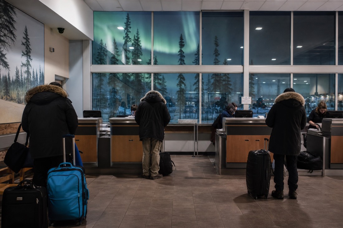 Rental car desks inside the small Yellowknife airport terminal with parkas and luggage in the foreground