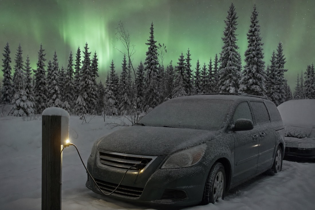 Block heater cord plugged into an outdoor power post beside a frost-covered car in a snowy Yellowknife parking lot