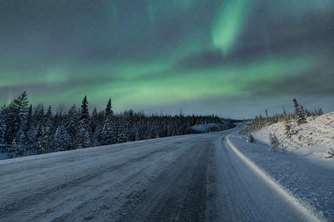 Empty snow-lined Ingraham Trail highway curving through spruce forest under a low winter sun east of Yellowknife