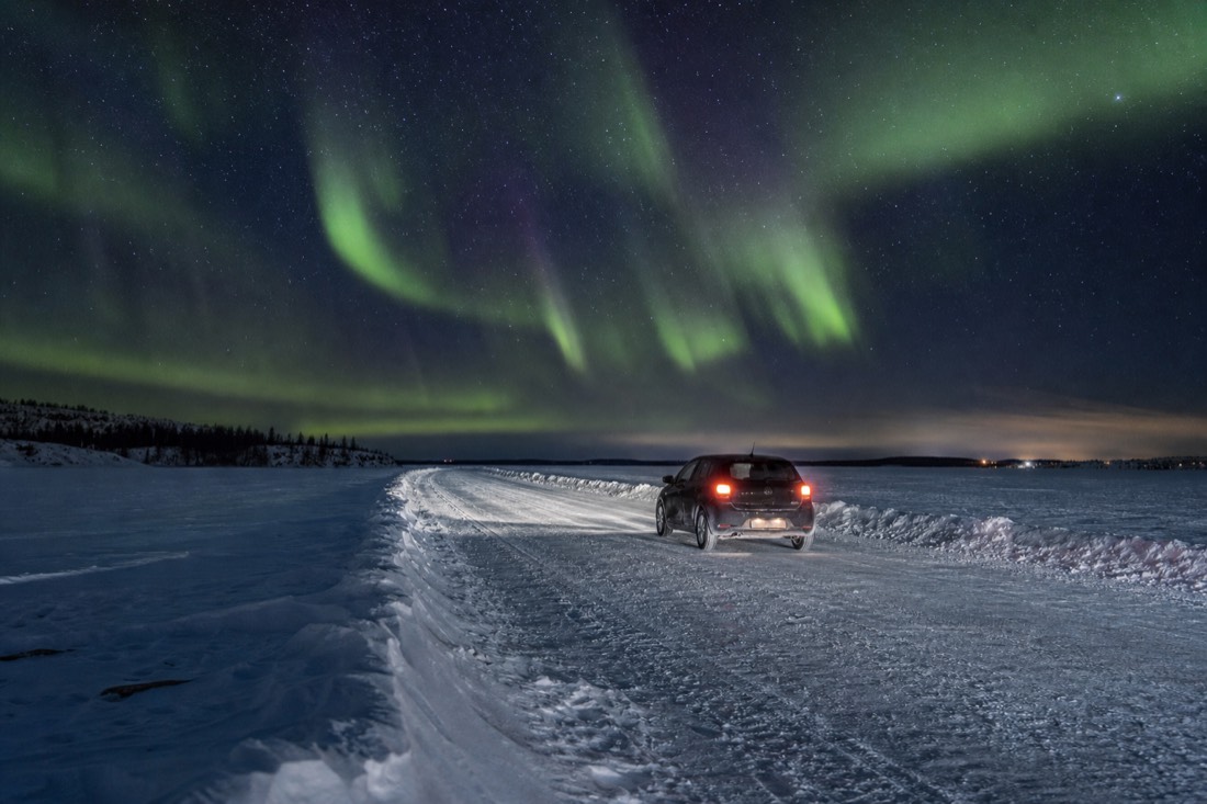 Compact car crossing the plowed Dettah ice road over the frozen Yellowknife Bay with snowbanks marking the lane