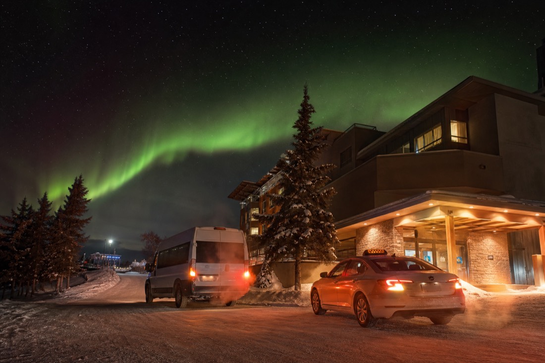 Tour van and a taxi waiting outside a downtown Yellowknife hotel on a cold winter evening with exhaust rising