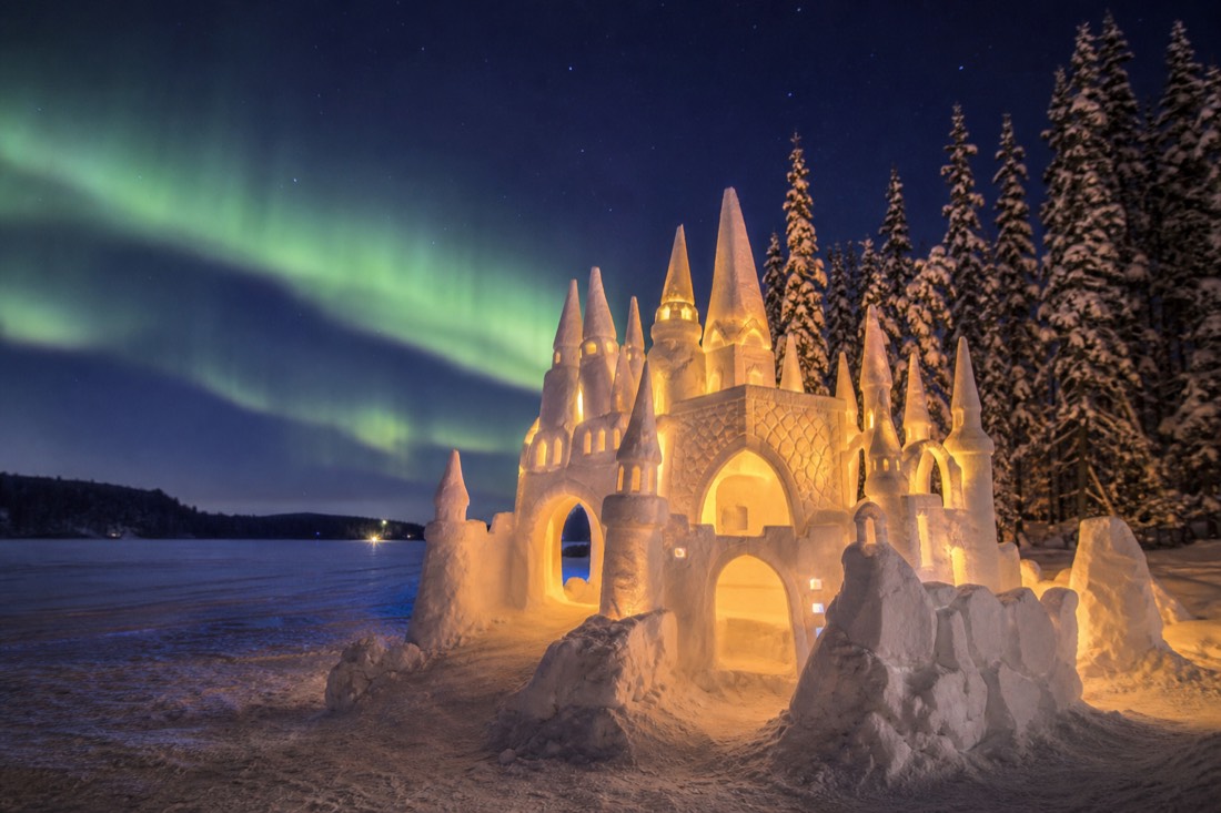 A carved snow castle glowing at dusk on frozen Yellowknife Bay during the SnowKing Winter Festival