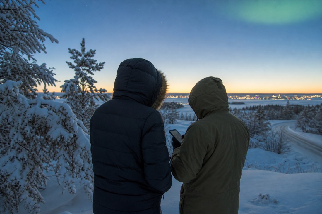 Travelers in heavy parkas checking a phone weather forecast on a bright frigid Yellowknife morning