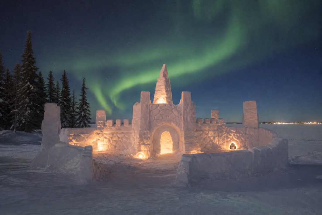 Carved snow castle glowing at dusk on frozen Yellowknife Bay during the SnowKing Winter Festival