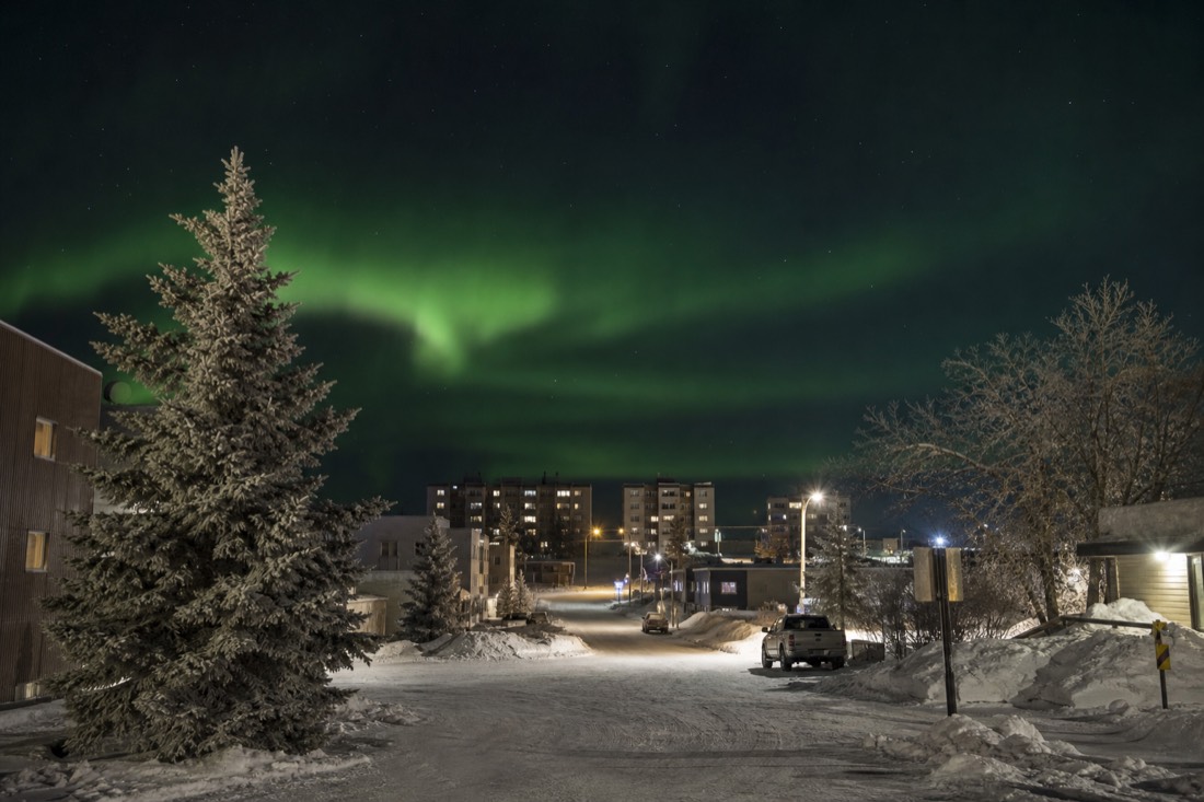 Quiet snow-covered downtown street in Yellowknife at midday with low golden light and parked winterized cars