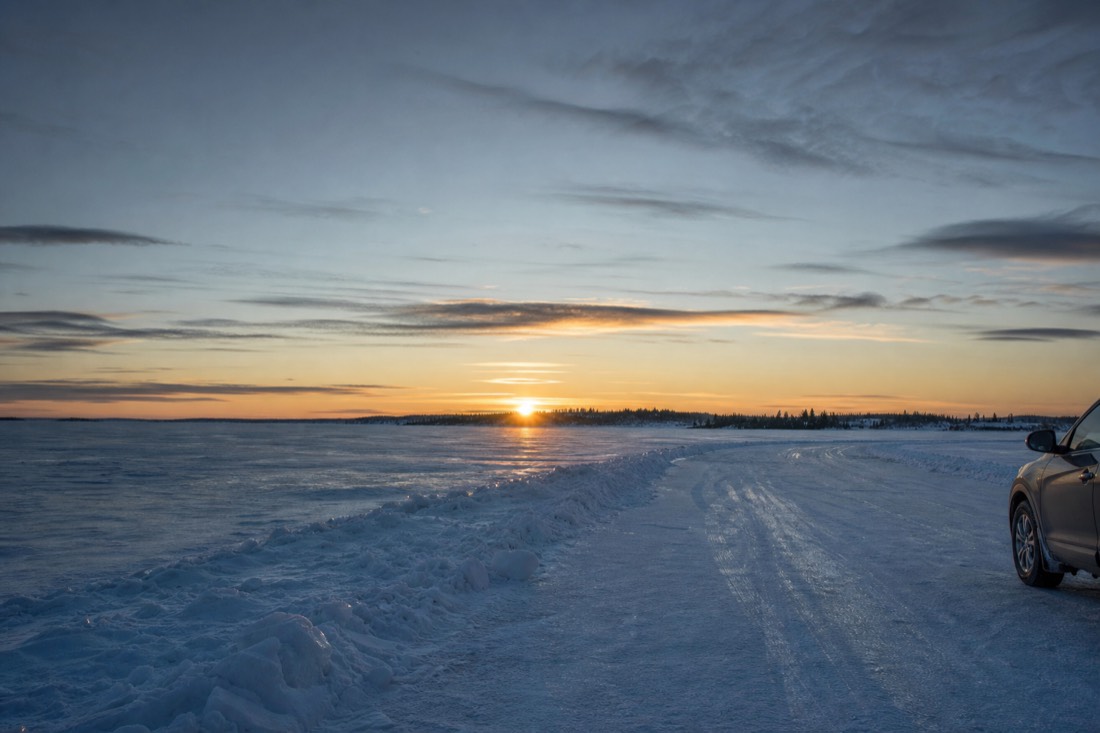 Frozen Yellowknife Bay in early spring with a plowed ice road lane, bare lake ice and a low sun over the far shore