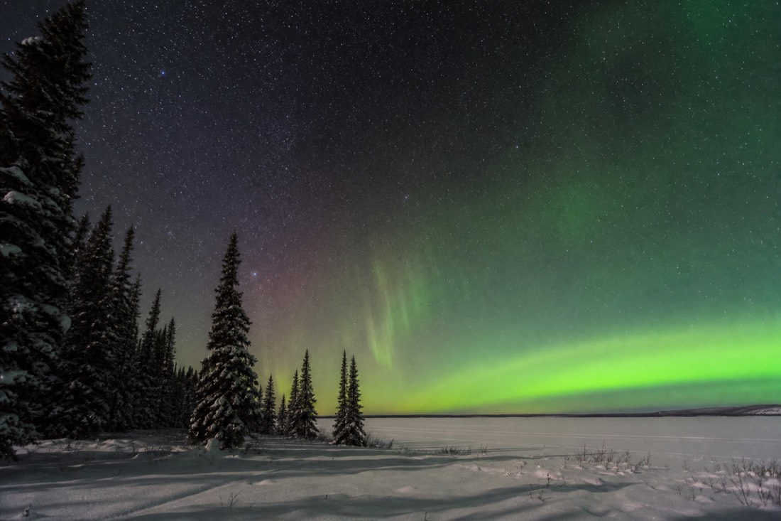 Crisp starfield and rising aurora over a flat white horizon of lake ice with no mountains in view