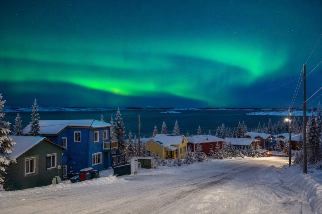 Colourful wooden houses and a snow-covered road in Old Town Yellowknife with Great Slave Lake behind